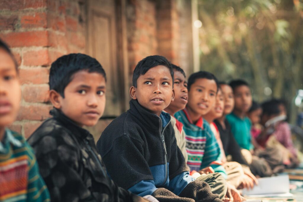 A group of children from Bangladesh sitting outdoors, engaged in learning at a rural school.