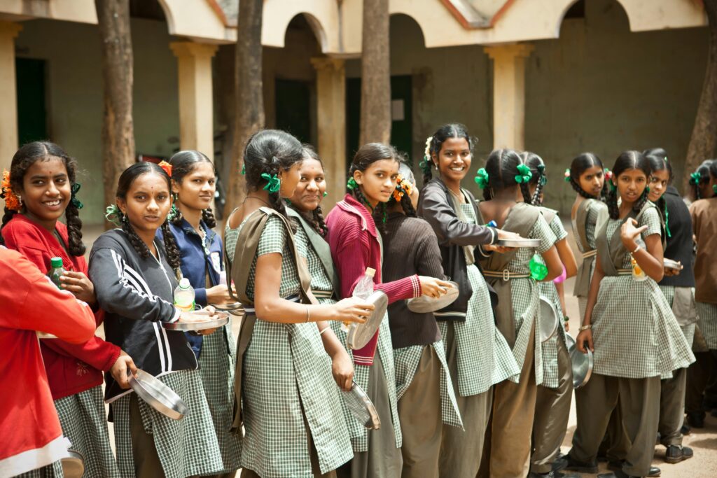 Group of smiling schoolgirls with braids standing outdoors during lunchtime at school.